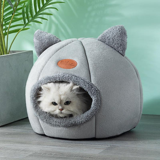 Cute furry cat resting in soft gray cave-shaped bed. The bed has cute fluffy ears